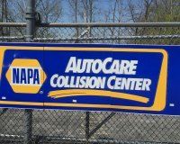 A napa autocare collision center sign is hanging on a chain link fence.