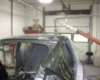 A car is being dismantled in a garage with a crane.