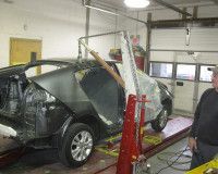 A man is standing next to a car that is being repaired in a garage.