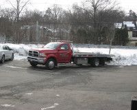 A red tow truck is parked in a parking lot next to a snowy field.