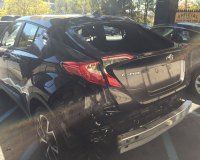 A black car with a damaged rear end is parked in a parking lot.