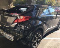 A black car with a damaged rear end is parked in a parking lot.