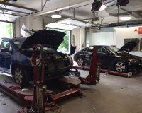 Two cars are being worked on in a garage with their hoods open.