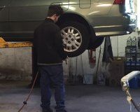 A man is standing next to a car on a lift in a garage.