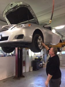 A man is standing next to a car on a lift in a garage.