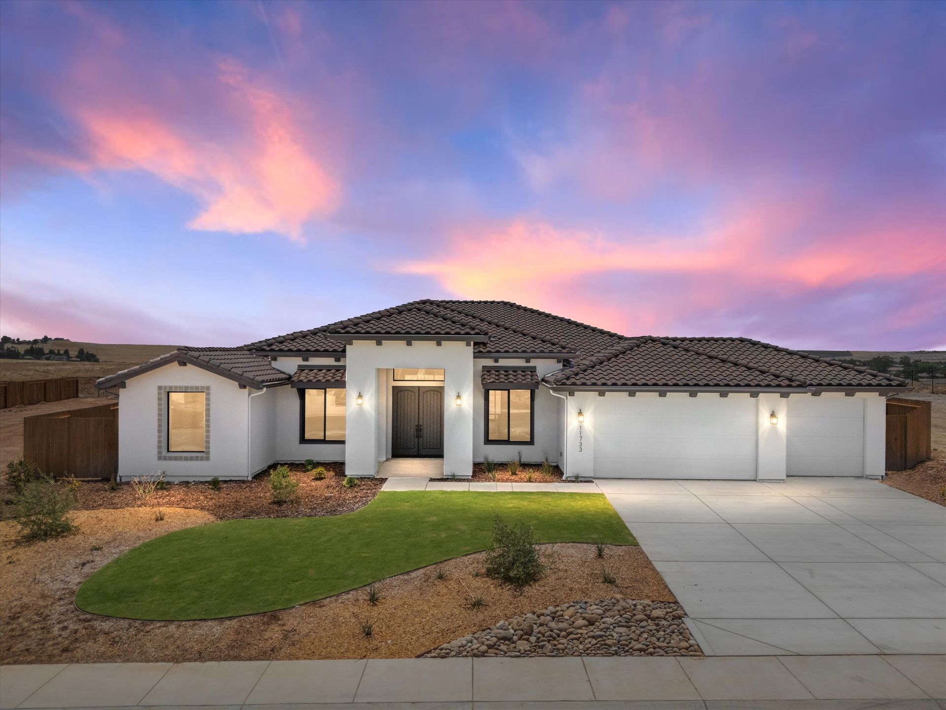 Modern white house with dark trim, tile roof, and a sunset sky.