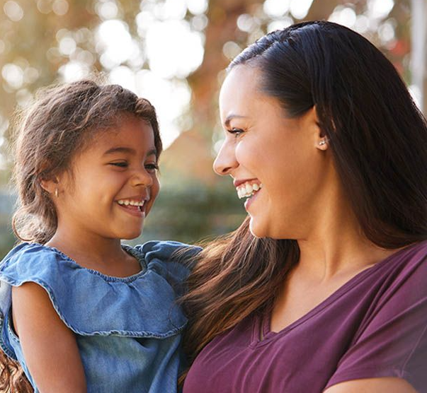 A woman is holding a little girl in her arms and smiling at her.