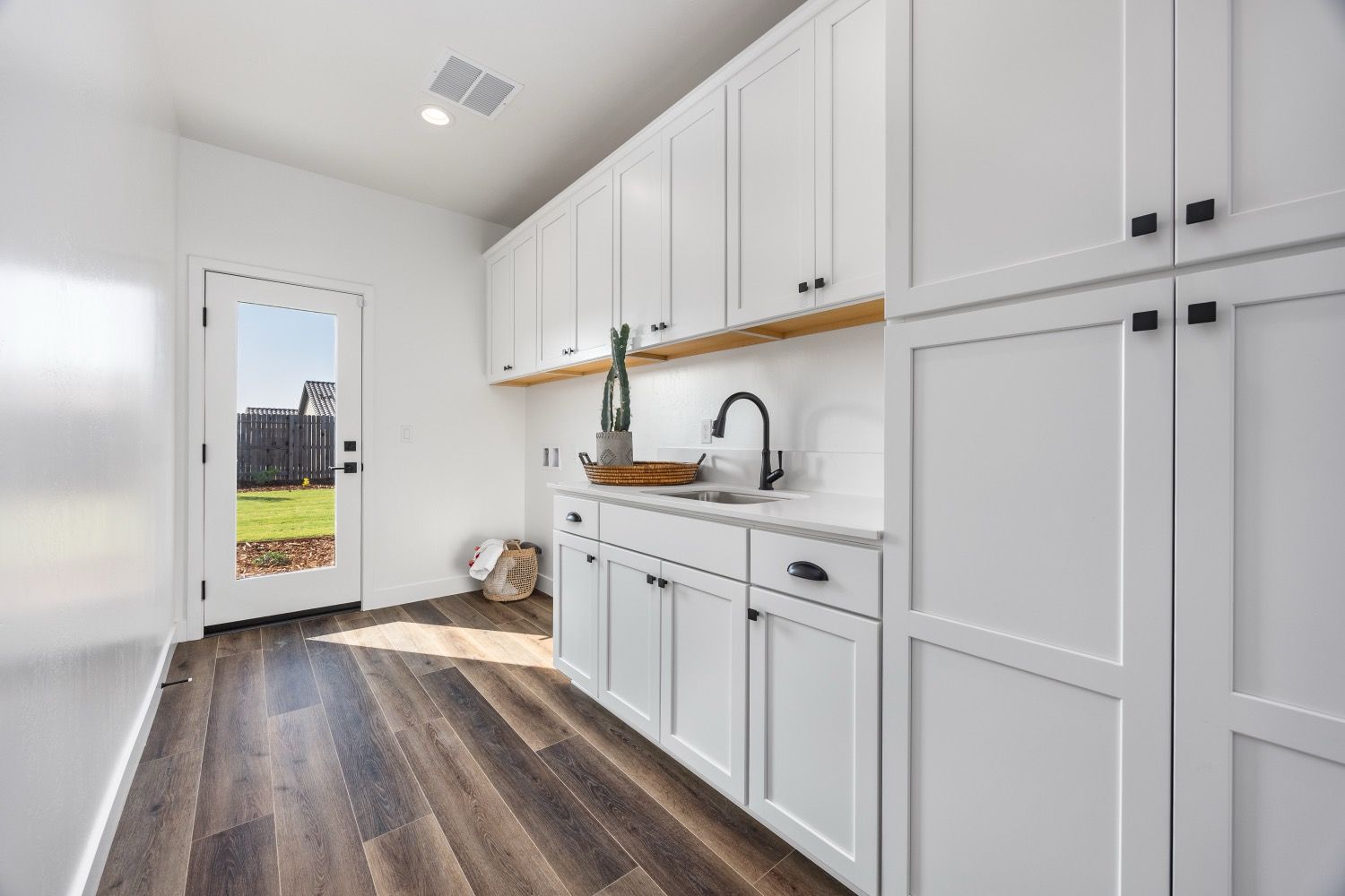 Laundry room with white cabinets, dark hardware, and a sink. Door leads outside.