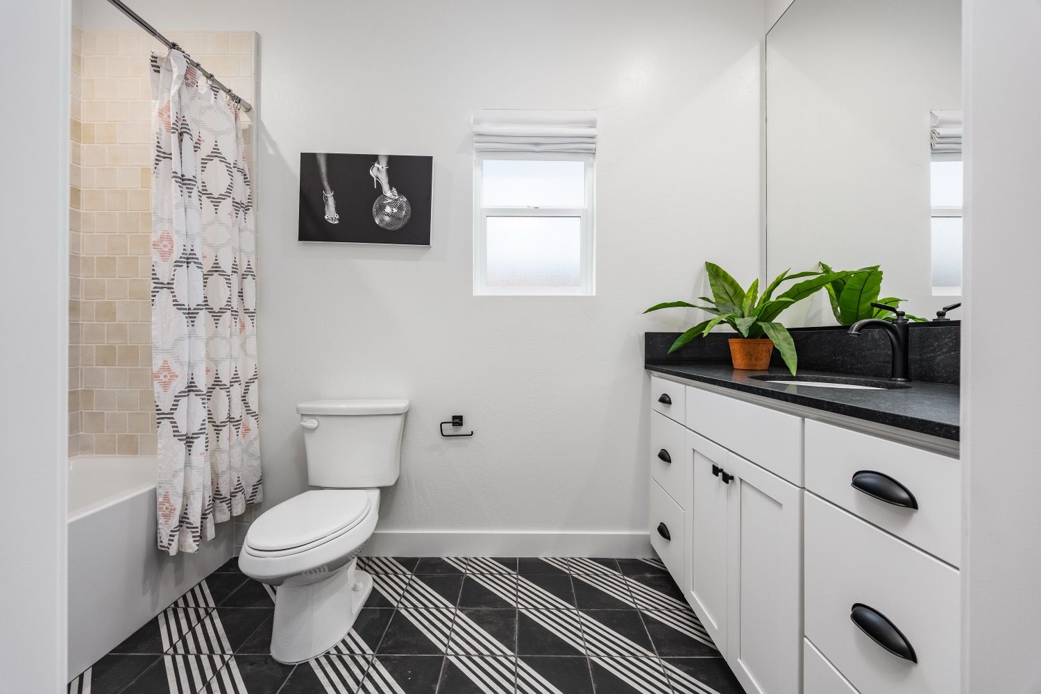 Bathroom with white vanity, black countertop, patterned floor, and shower.