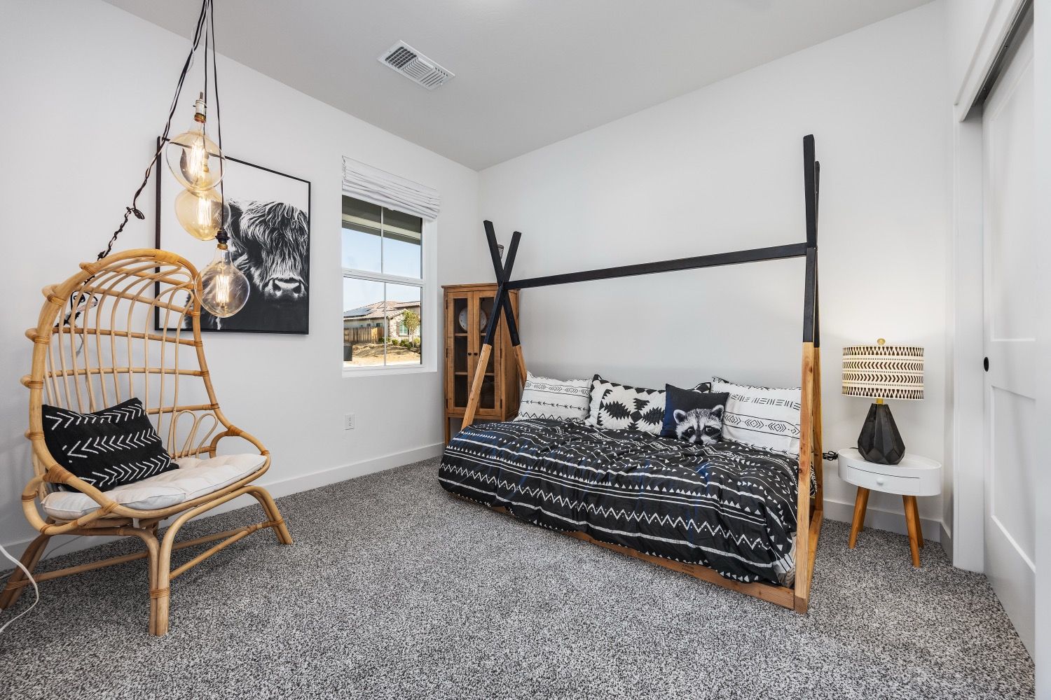 Bedroom with a rattan chair, black teepee bed, neutral rug, and decorative lighting.
