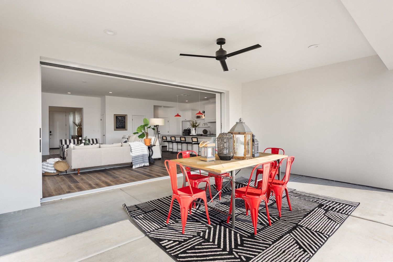 Open-air dining area with a wood table, red chairs, and a black and white rug, leading into a living space.
