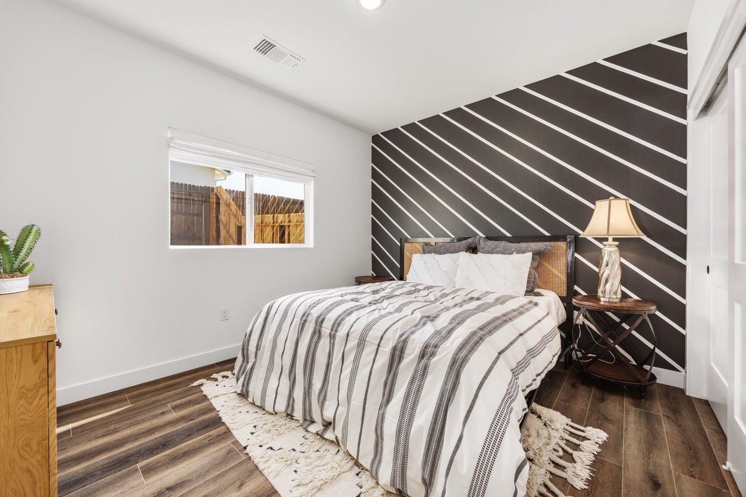 Bedroom with bed, patterned wall, wood floor, side table with lamp, and window.