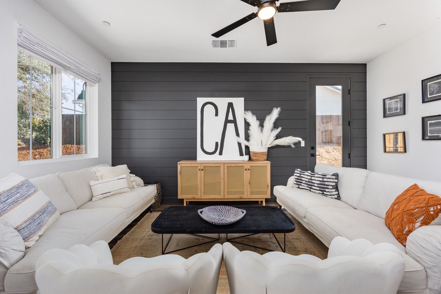 Living room with white sofas, black accent wall, and wooden cabinet.