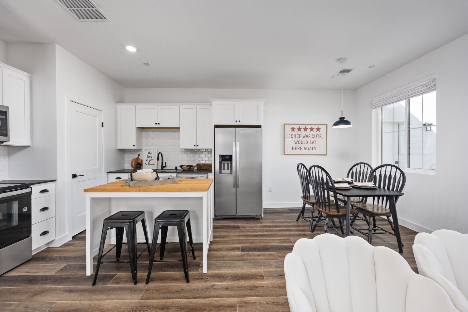Open-plan kitchen and dining area with white cabinets, stainless steel appliances, and a wooden table with black stools.