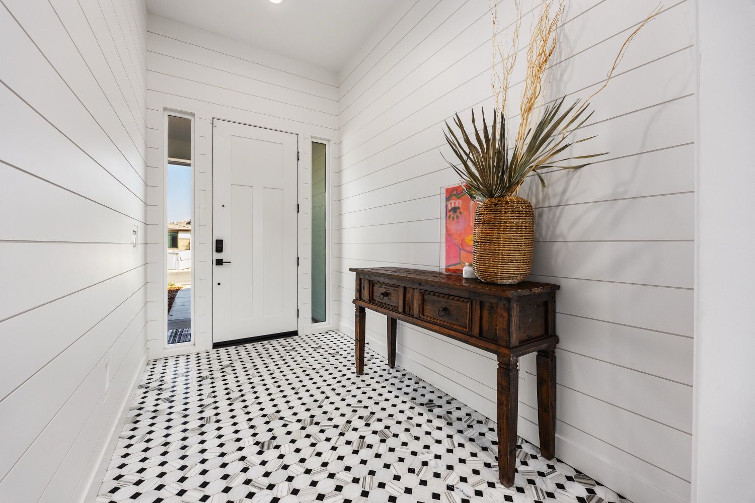 Entryway with white plank walls, black and white patterned tile floor, and a dark wood console table with a decorative vase.