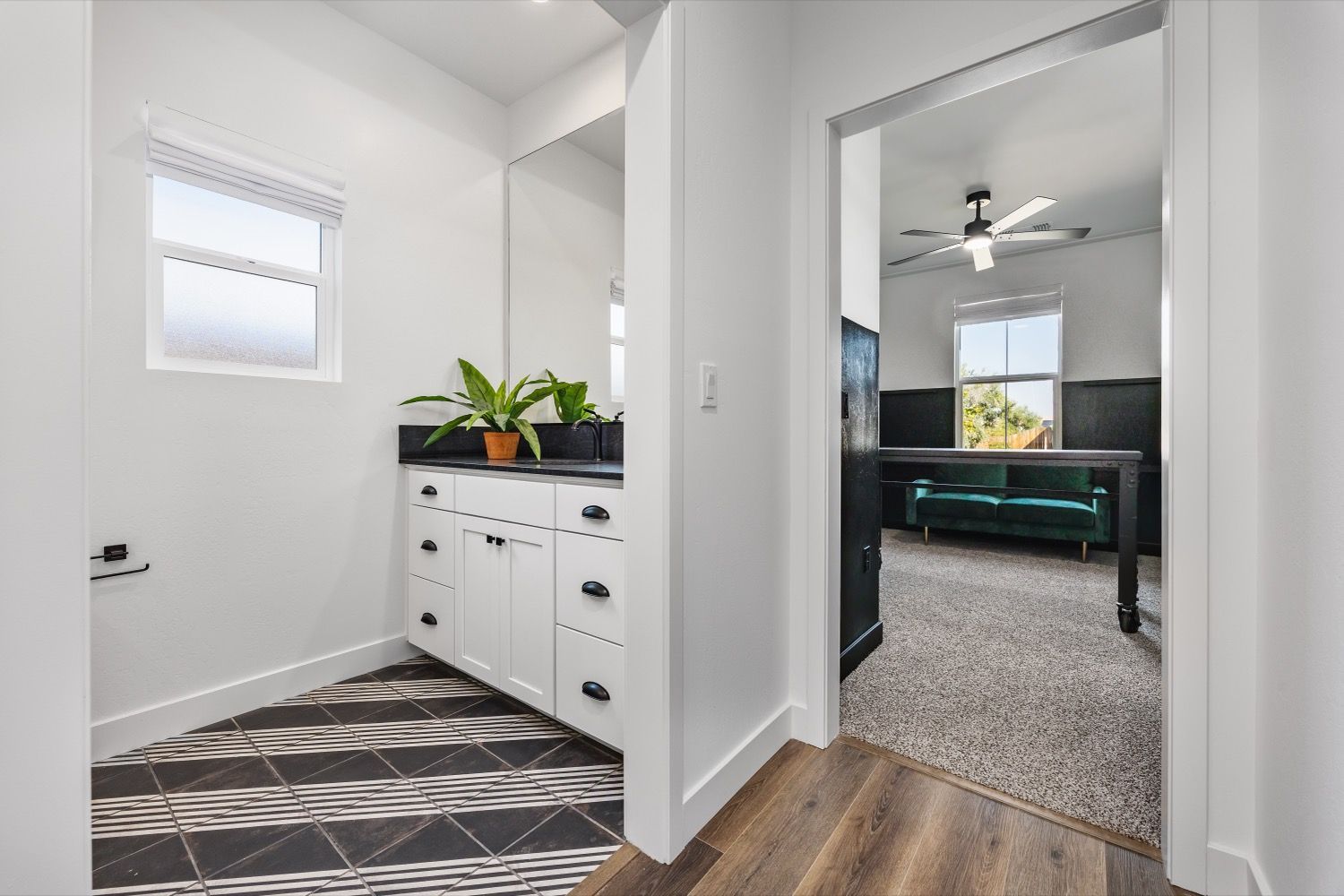 Bathroom with white cabinets, patterned floor, and doorway to a room with a sofa and ceiling fan.