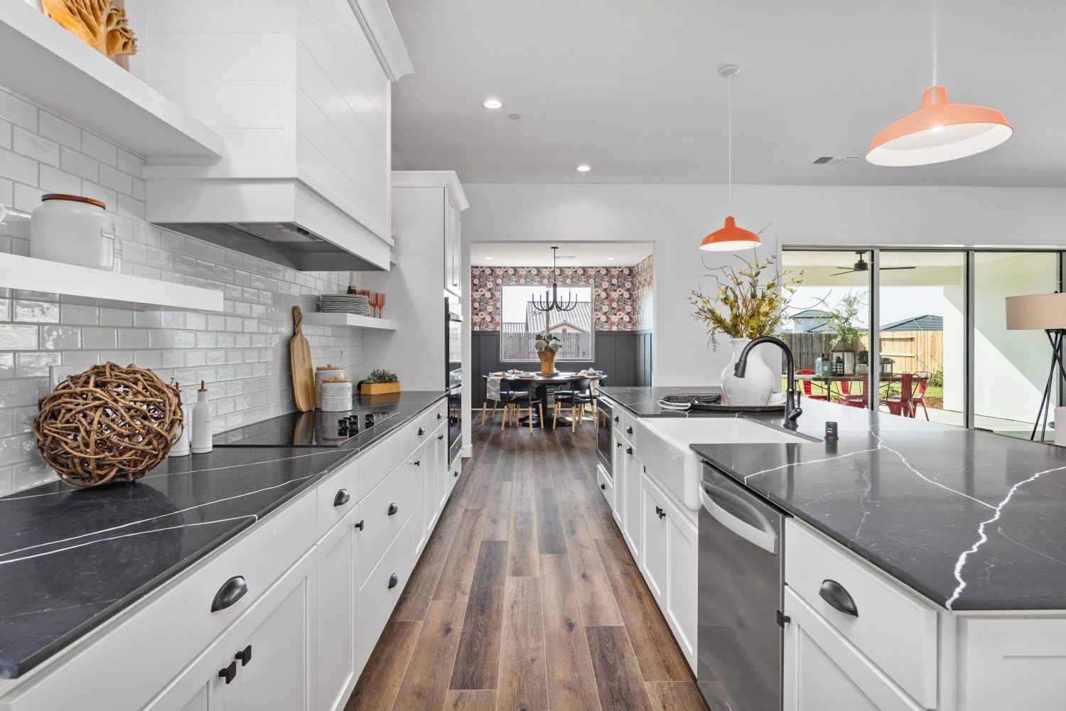 Modern kitchen with white cabinets, dark countertops, and orange pendant lights.