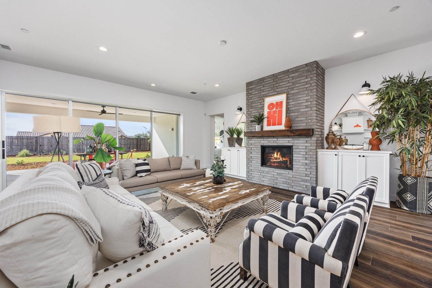 Living room with fireplace, sofas, and large windows overlooking a backyard. Black and white striped accents.