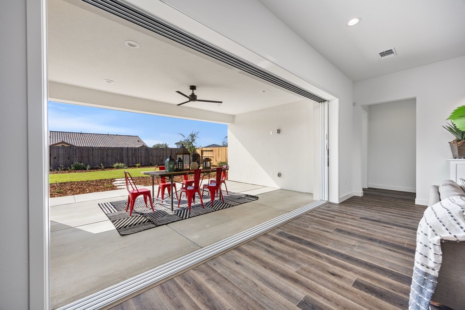 Open folding glass doors reveal a patio with red chairs, a table, and a yard with a fence.
