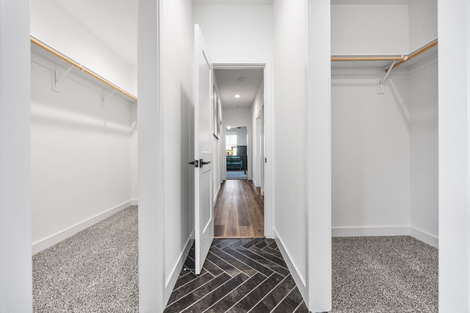 Walk-in closet with white walls and wooden floor. Empty shelves on the sides, an open door at the end.