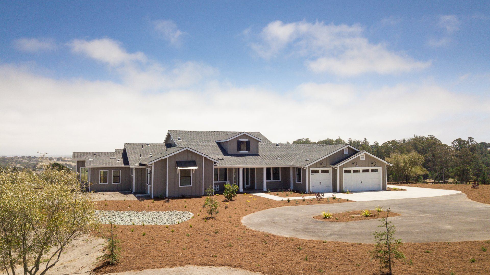 A large house with a gray roof is sitting on top of a dirt field.