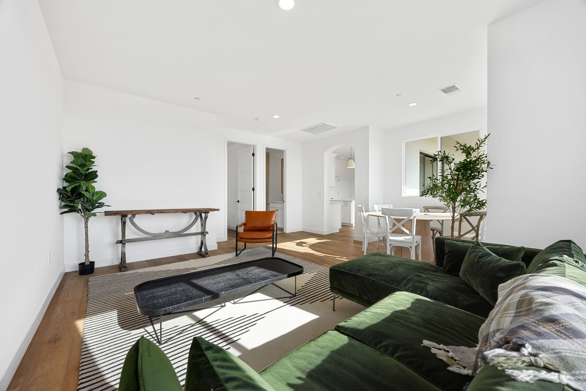 A bright living room with a green sectional, black rug, and a dining area visible.