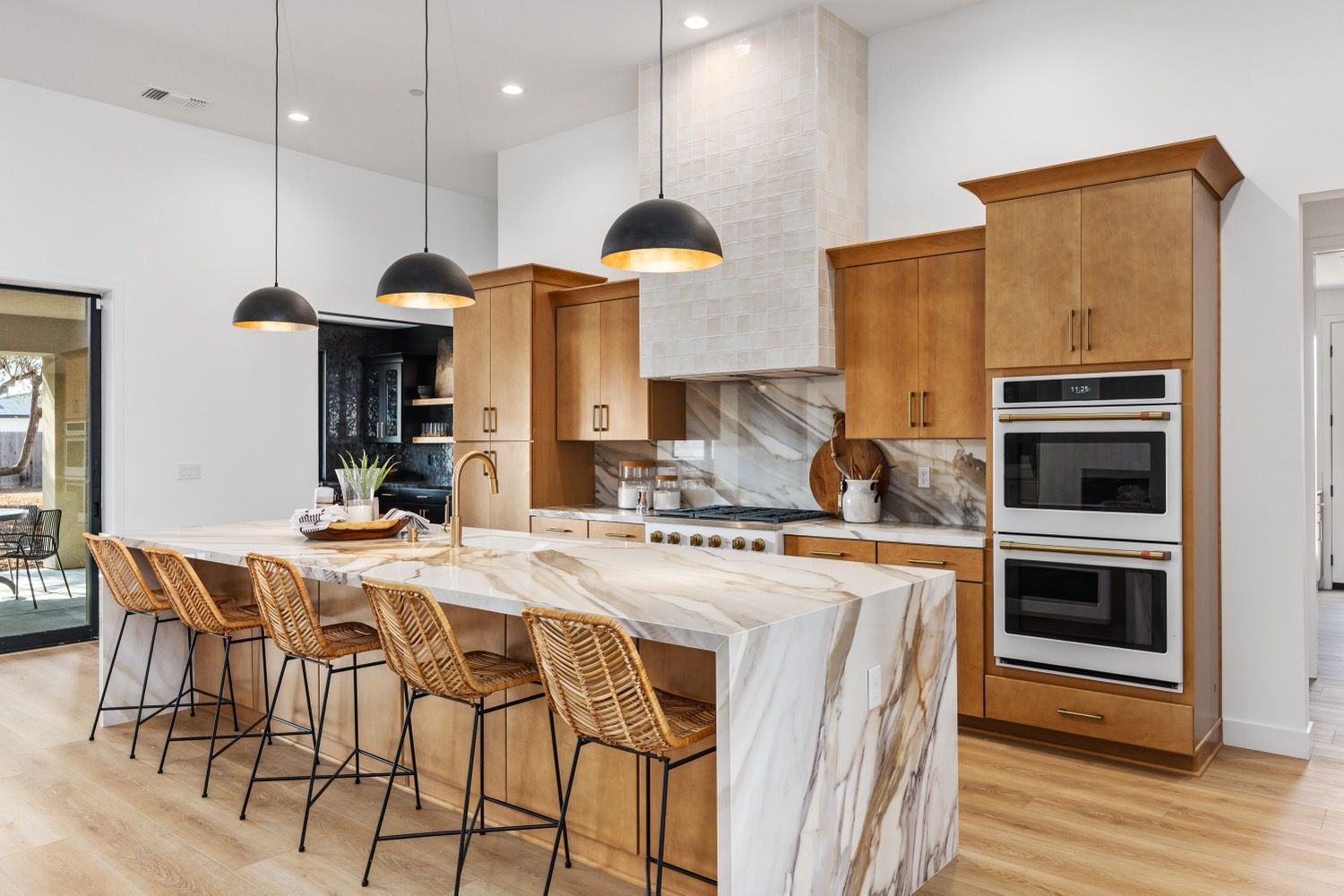 Modern kitchen with light wood cabinets, marble island with seating, and pendant lights.