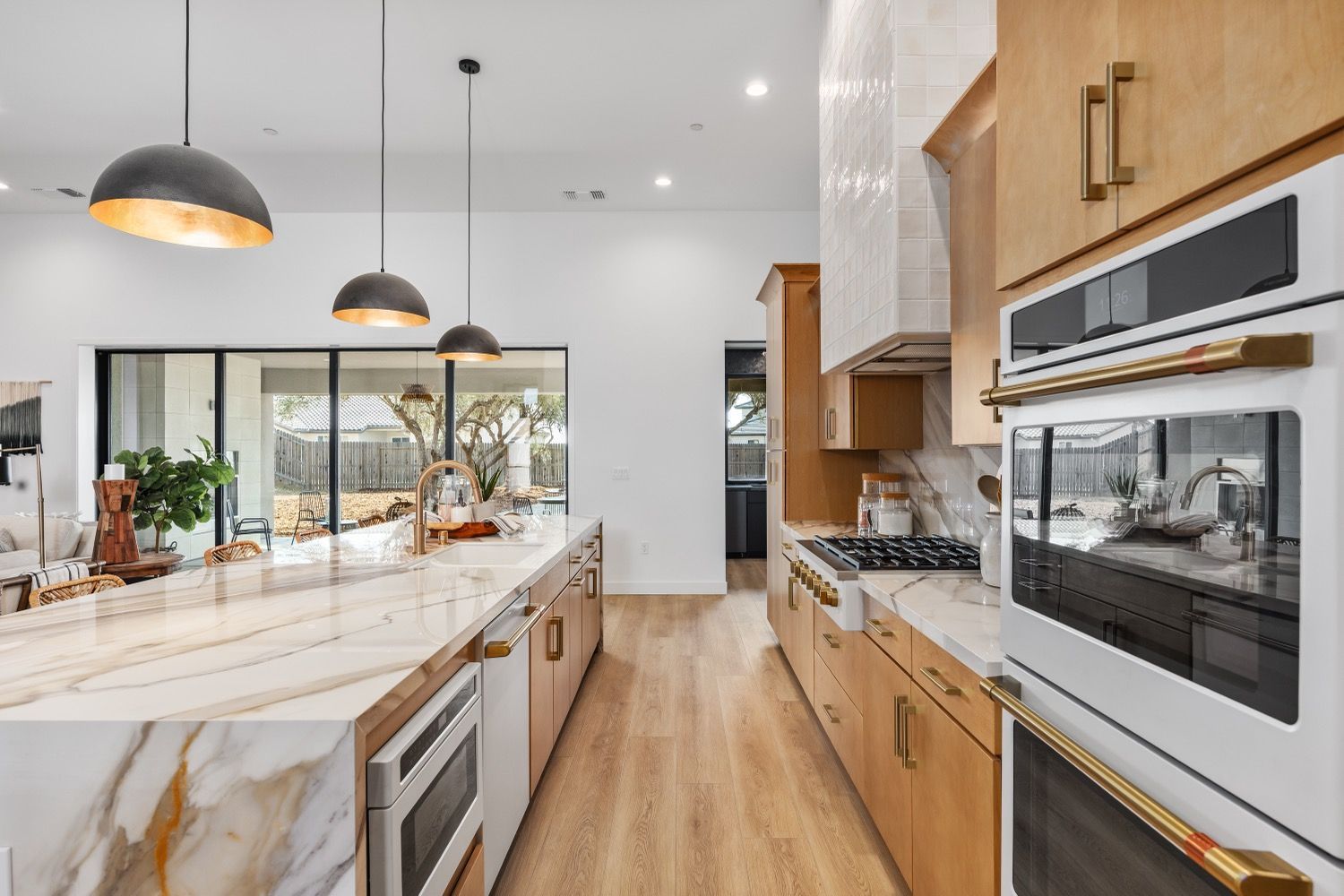 Modern kitchen with light wood cabinets, marble countertops, and gold accents.