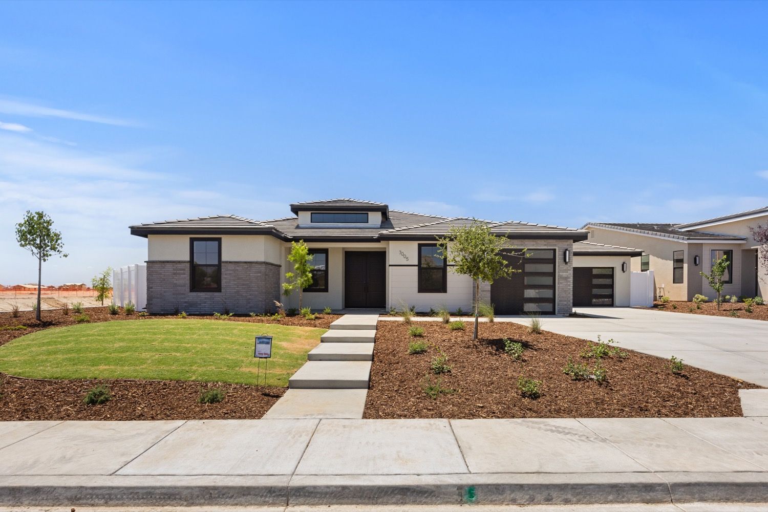 Modern single-story home with a manicured lawn, driveway, and landscaping on a sunny day.