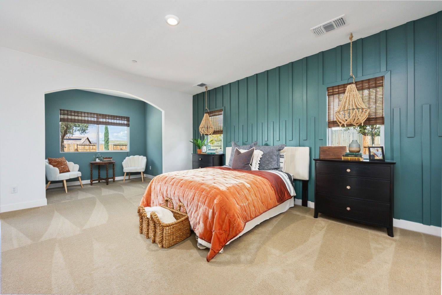 Bedroom with teal accent wall, bed, chairs, and large window overlooking a landscape.