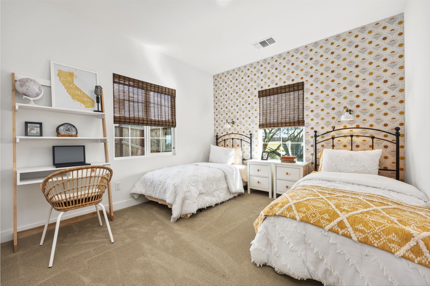 Bedroom with two beds, a desk, and a patterned accent wall. Beige carpet and white walls.