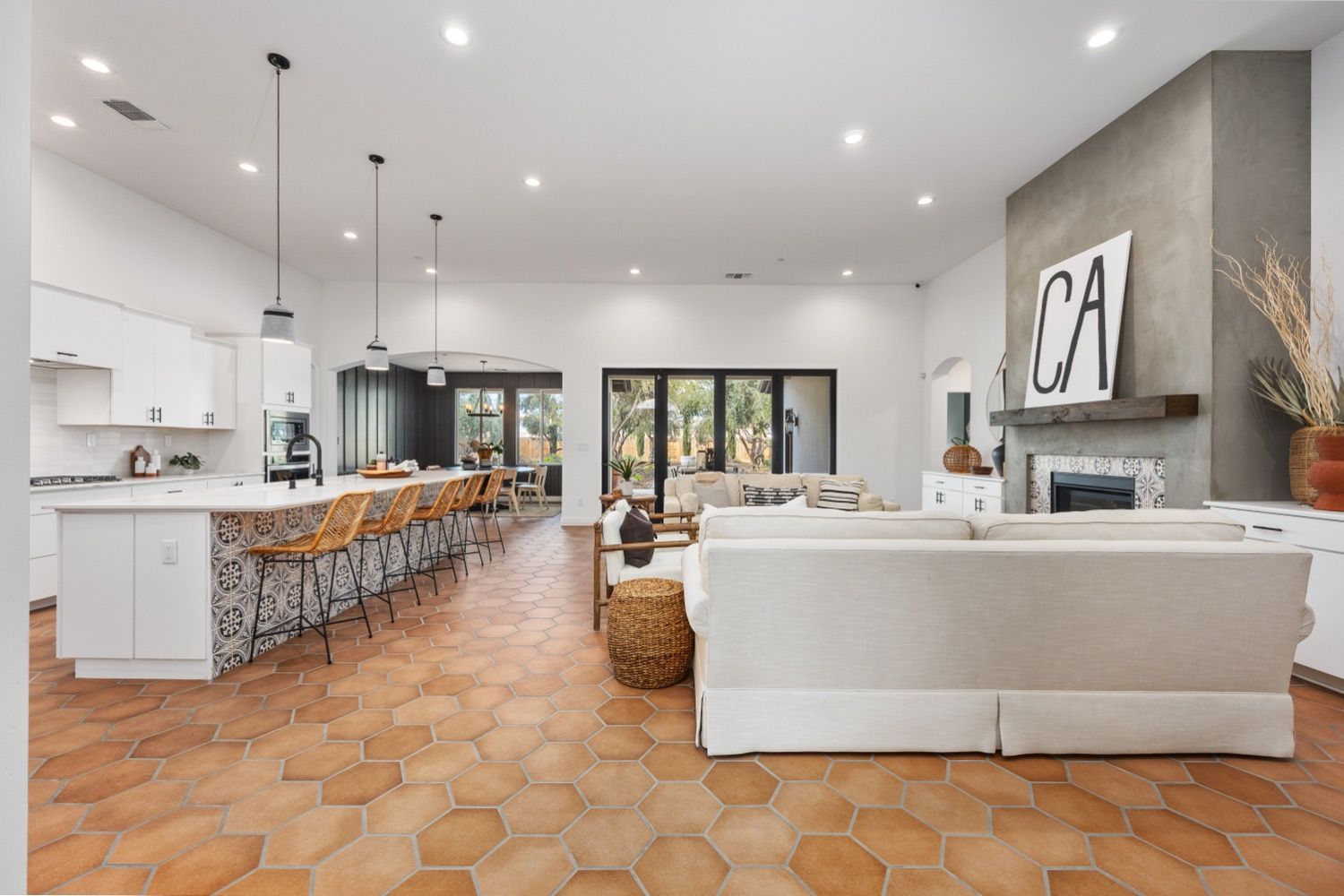Open-concept living space with kitchen, living area, and terracotta hexagon floor. Bright, modern design.