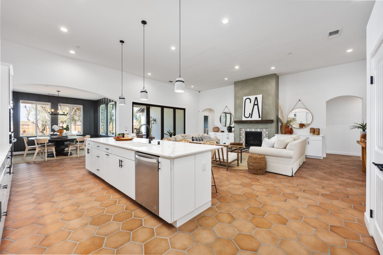 Spacious, open-plan kitchen and living area with white walls, terracotta floors, and large island.