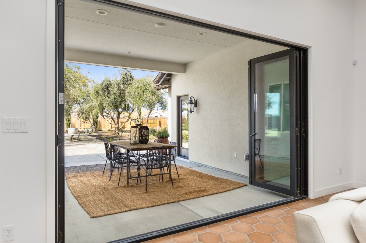 Large folding doors open to an outdoor dining area with a table, rug, and chairs.