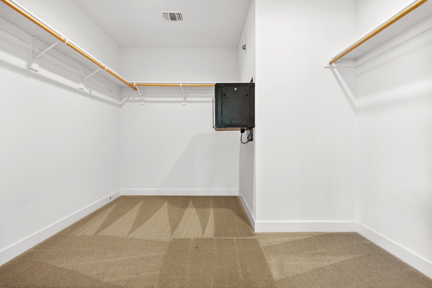 Empty walk-in closet with shelves and a mounted black TV. Beige carpet, white walls, and wood trim.