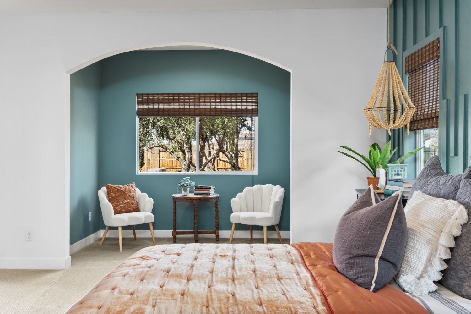 Bedroom interior with teal accent wall, window, chairs, and bed with decorative pillows and blanket.