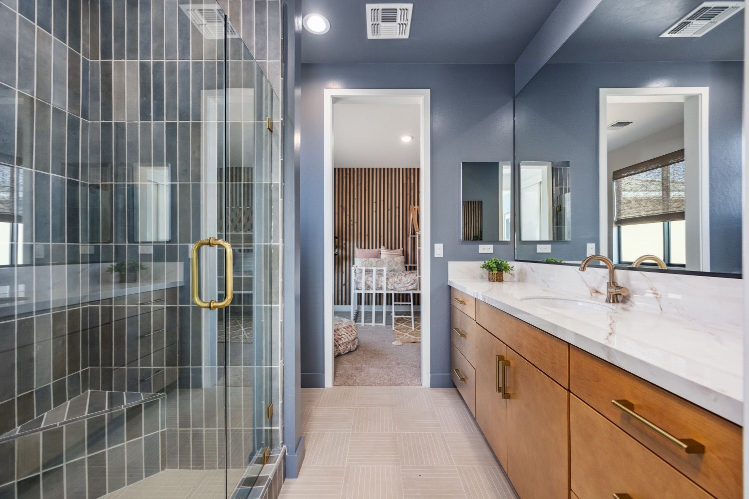 Modern bathroom with blue walls, wood vanity, glass shower, and view into bedroom.