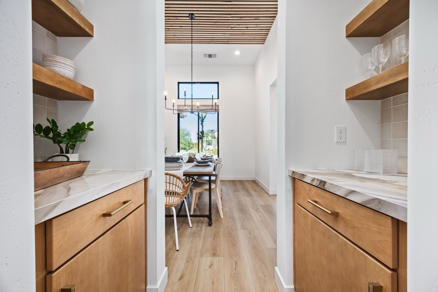 Hallway with shelves and cabinets on either side leading to a dining area with table and chairs.