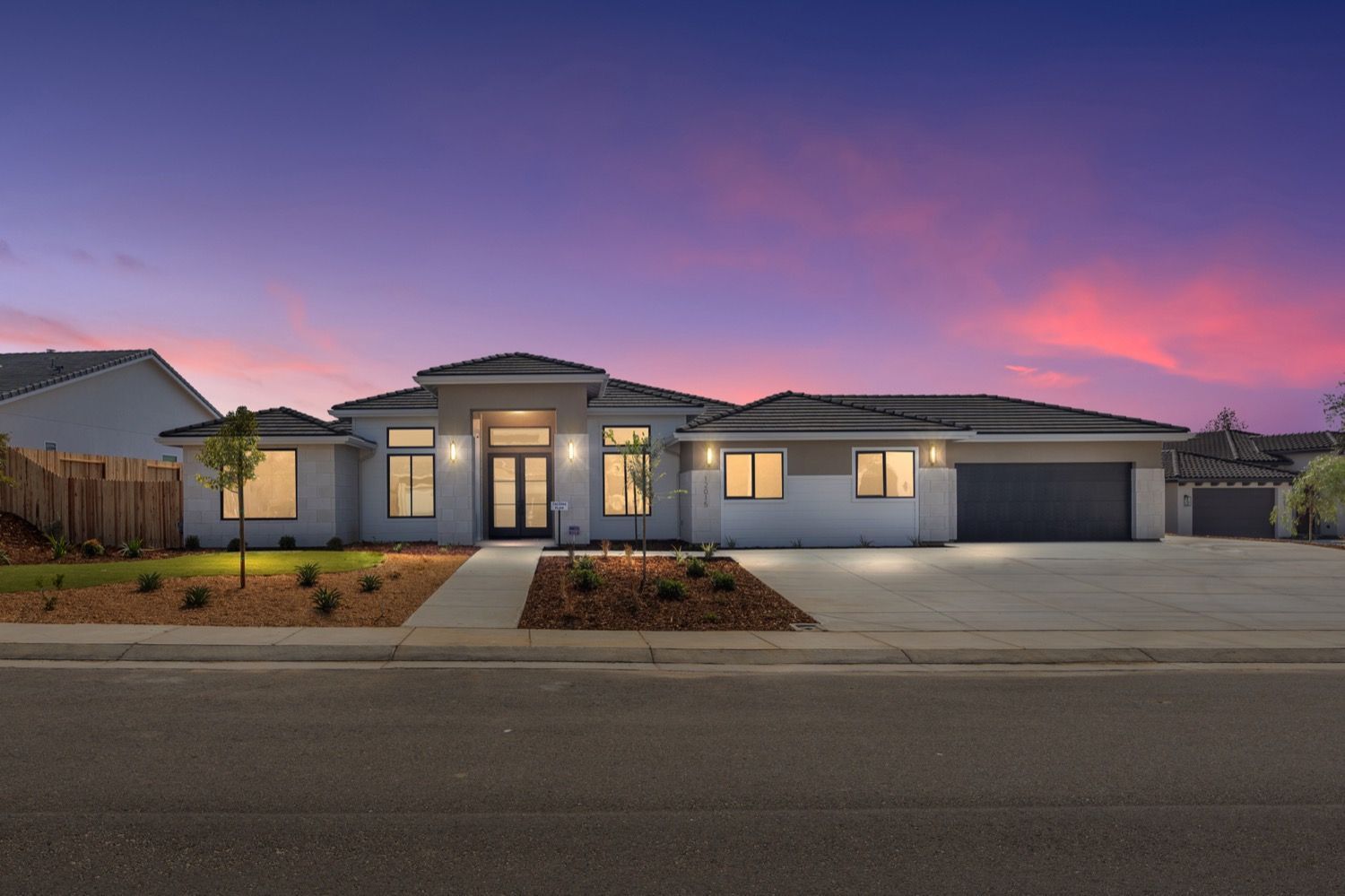 Modern single-story house with gray exterior and black garage door at dusk under a pink and purple sky.