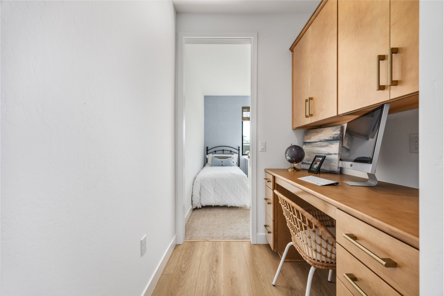 A home office with a desk and computer, looking into a bedroom with a bed.