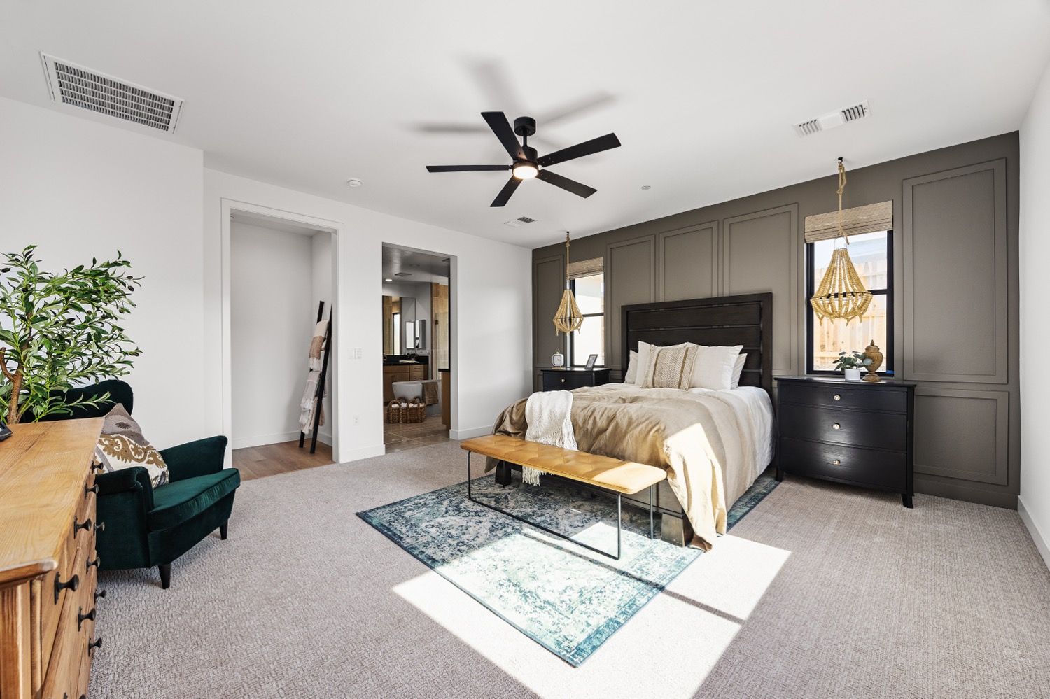 Spacious bedroom with gray carpet, a bed against a dark accent wall, and a sitting area with a green chair.