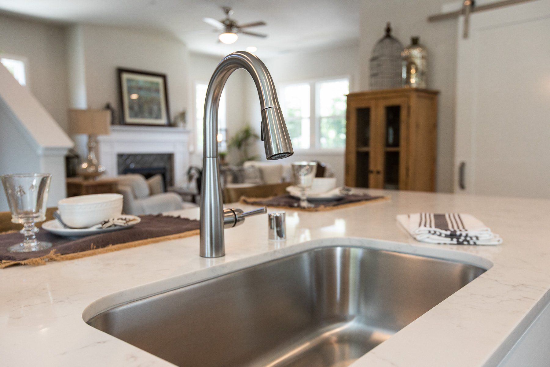 A kitchen sink with a faucet in a kitchen with a living room in the background.