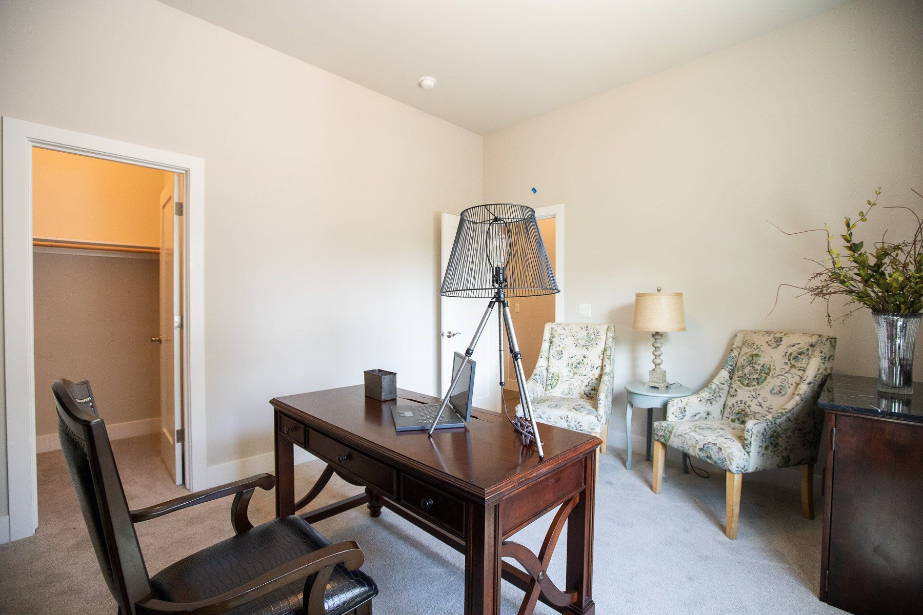 A home office with a desk , chairs and a lamp.