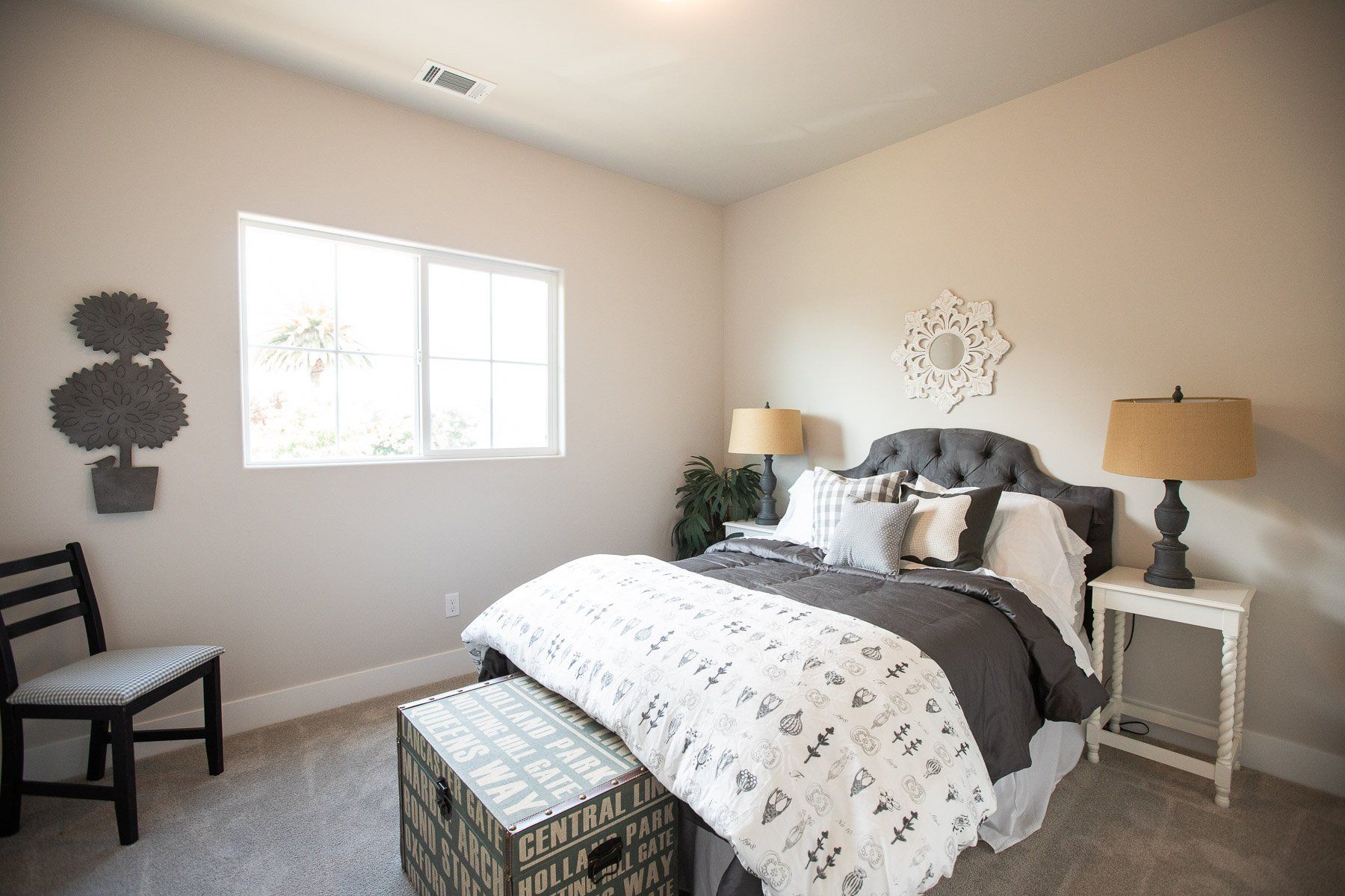 A bedroom with a bed , chair , nightstand , lamps and a window.