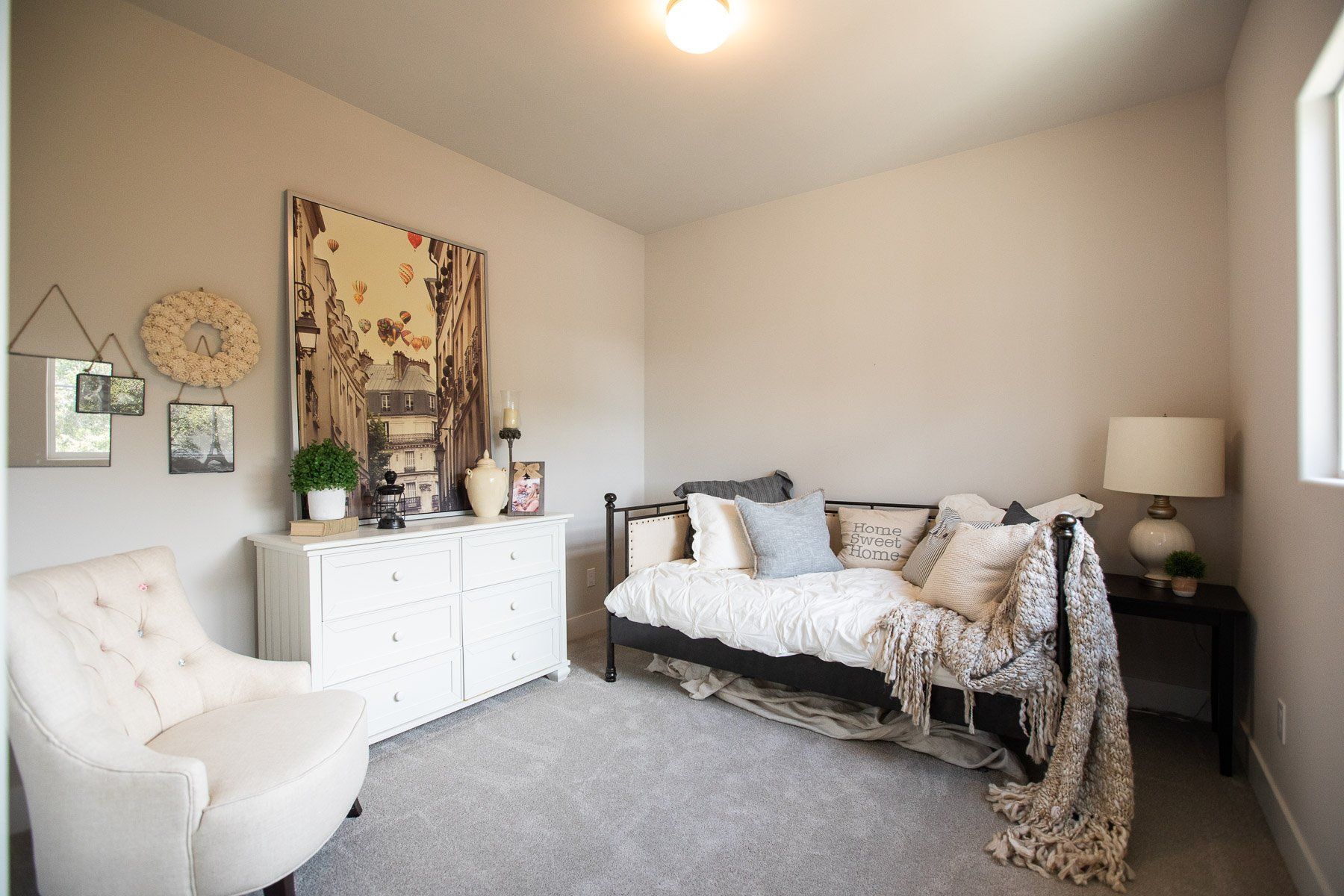 A bedroom with a day bed , chair , dresser and lamp.