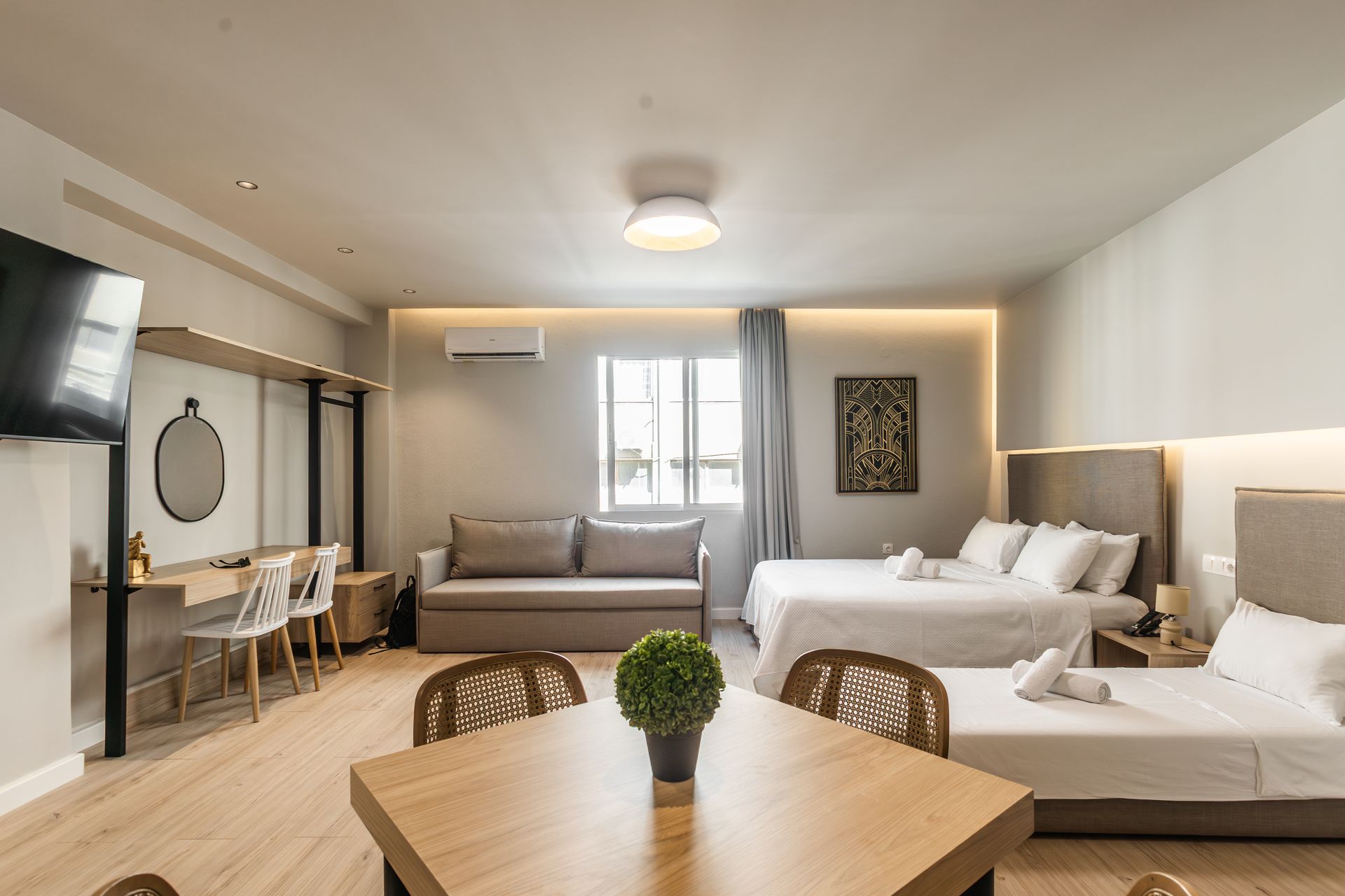 Modern hotel room with three beds, a sofa, and a table.
