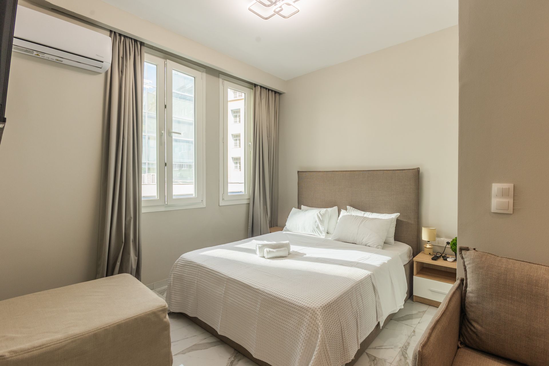 Bedroom with a double bed, windows with curtains, side table, and a small sofa.