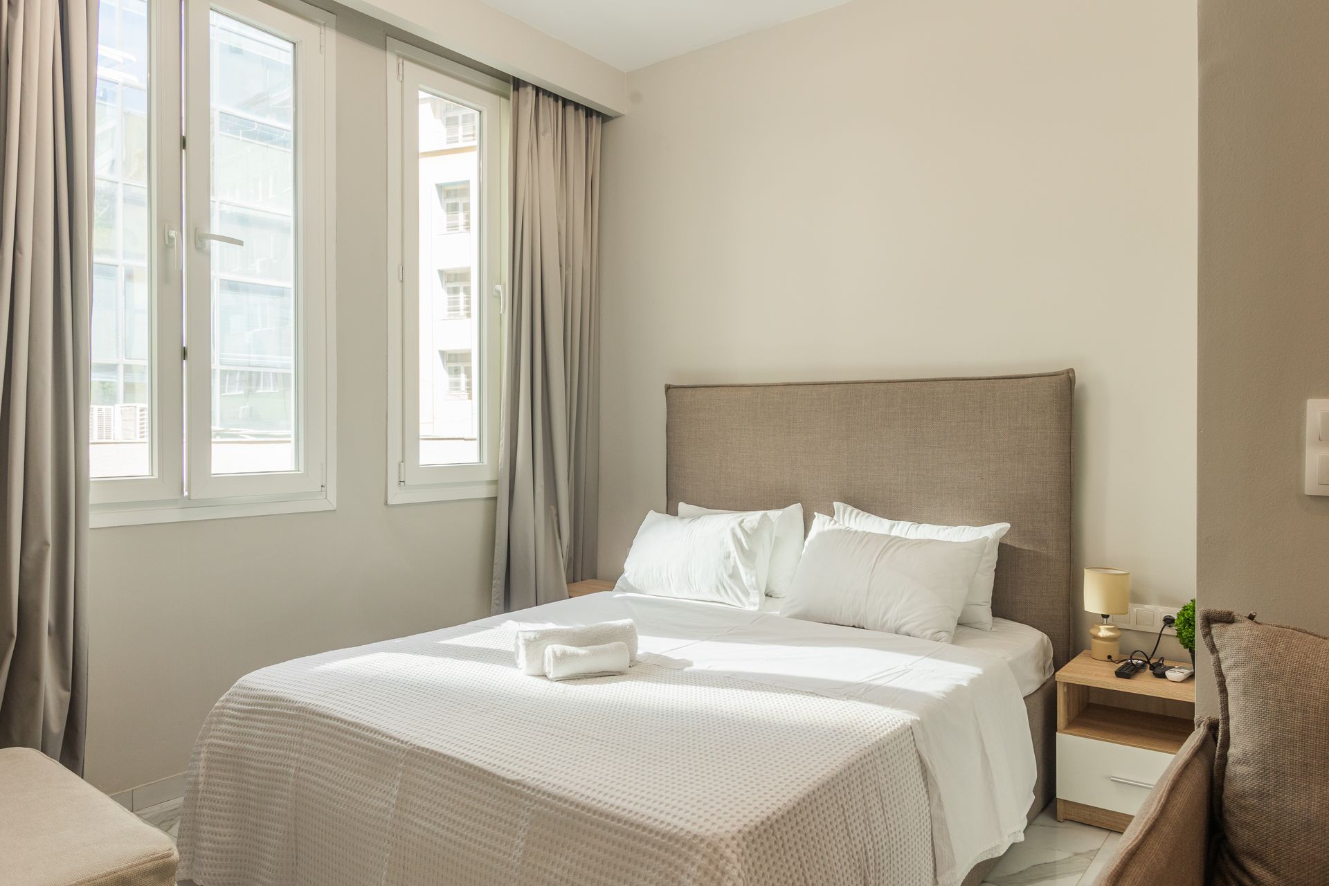 Bedroom with a double bed, two windows, and nightstand. Sunlight streams in, illuminating the space.