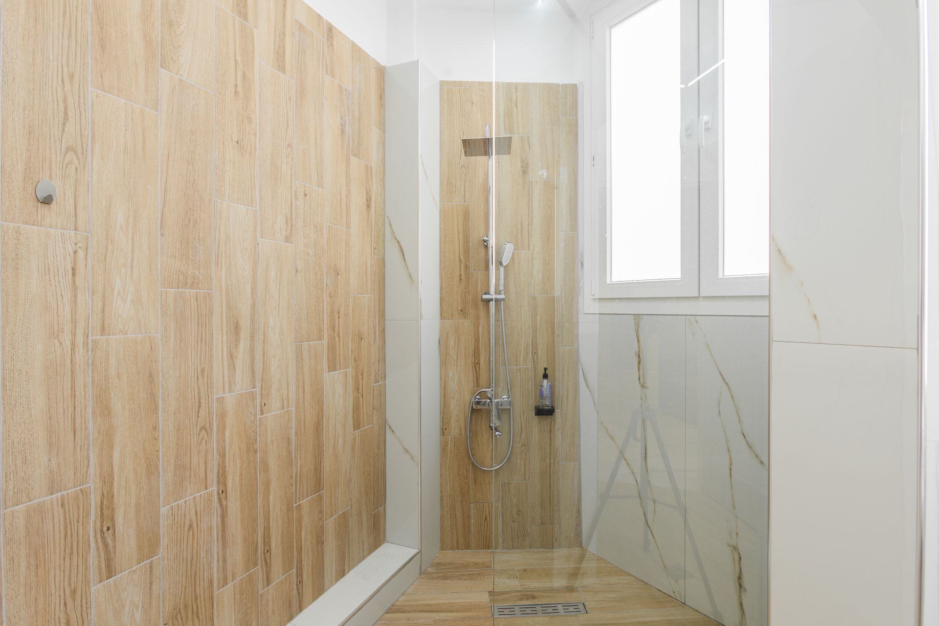 Shower with beige and white tile, glass door, and silver shower fixtures.