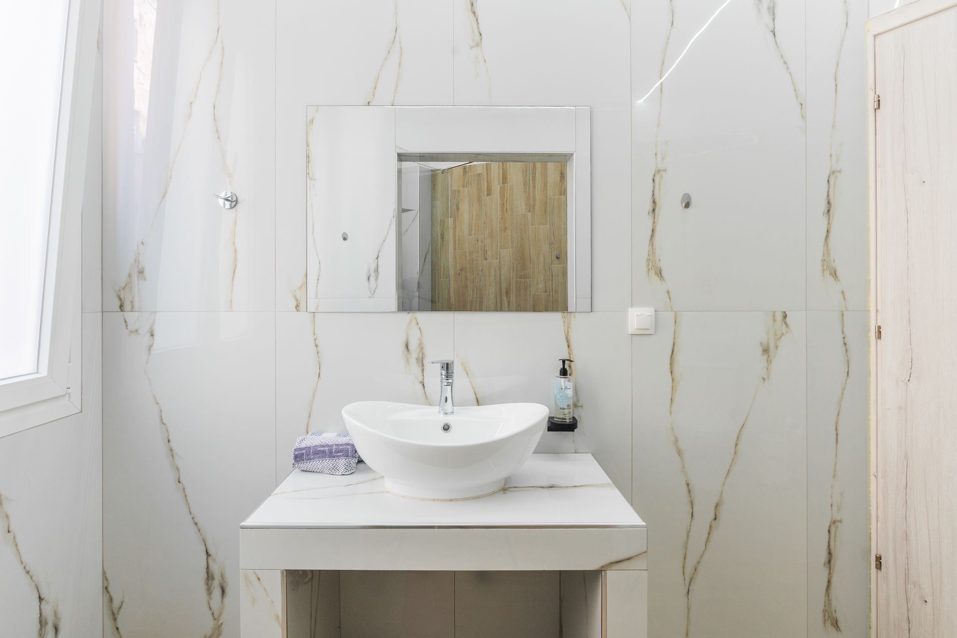 White bathroom with a modern sink, mirror, and marble-like tile.